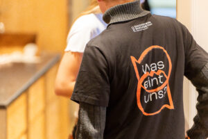 Person mit schwarzem T-Shirt mit der Aufschrift ‚Was eint uns?‘ Dachstein Dialoge 2024