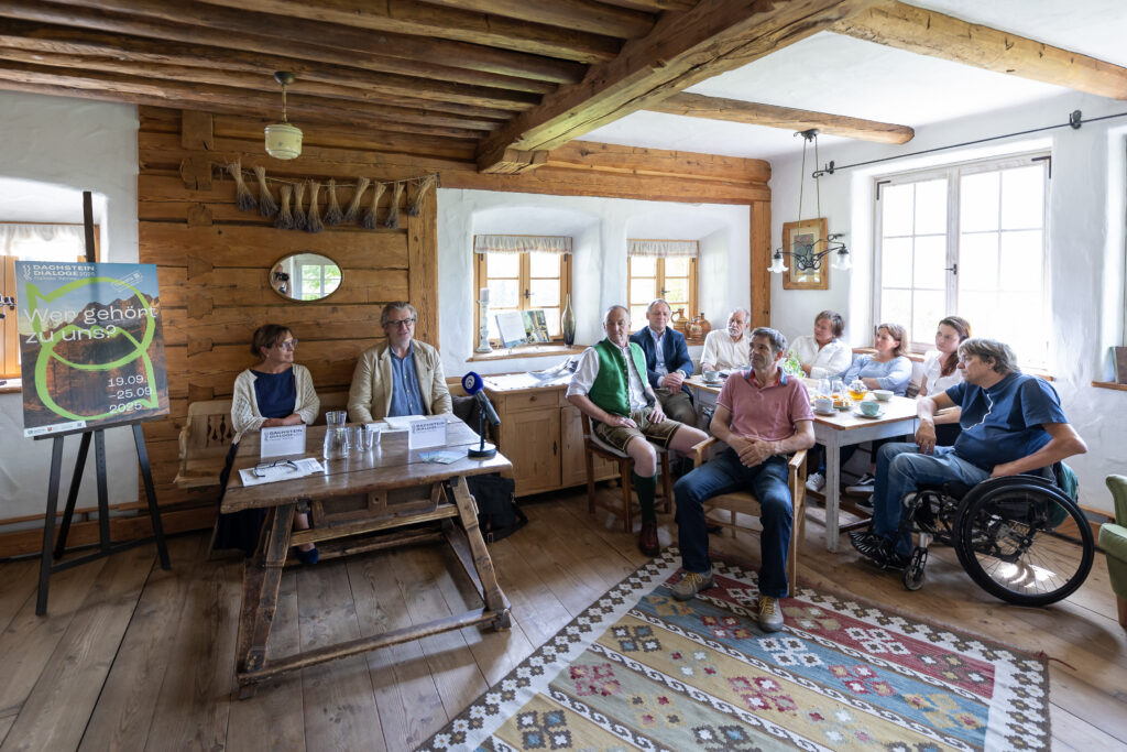 Pressegespräch vom 4.6.2025 - auf dem Foto sind Dachstein Dialoge Obfrau Frau Regina Stocker und Dachstein Dialoge Intendant Herr Philipp Blom zu sehen und weitere acht Menschen rund um einen Tisch, die ihnen zuhören